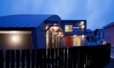 （東京都あきる野市）武蔵増戸のR屋根の家 (木杭を利用した柵から光がもれる夕景)
