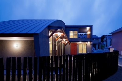 （東京都あきる野市）武蔵増戸のR屋根の家 (木杭を利用した柵から光がもれる夕景)