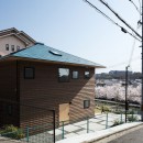 四つ角の家｜４つの小屋と立体路地の家｜大阪府堺市｜新築一戸建て住宅の写真 北西から見る。桜並木の先はなだらかな丘陵。アプローチは建物のかたちを踏襲した正方形のコンクリート土間。