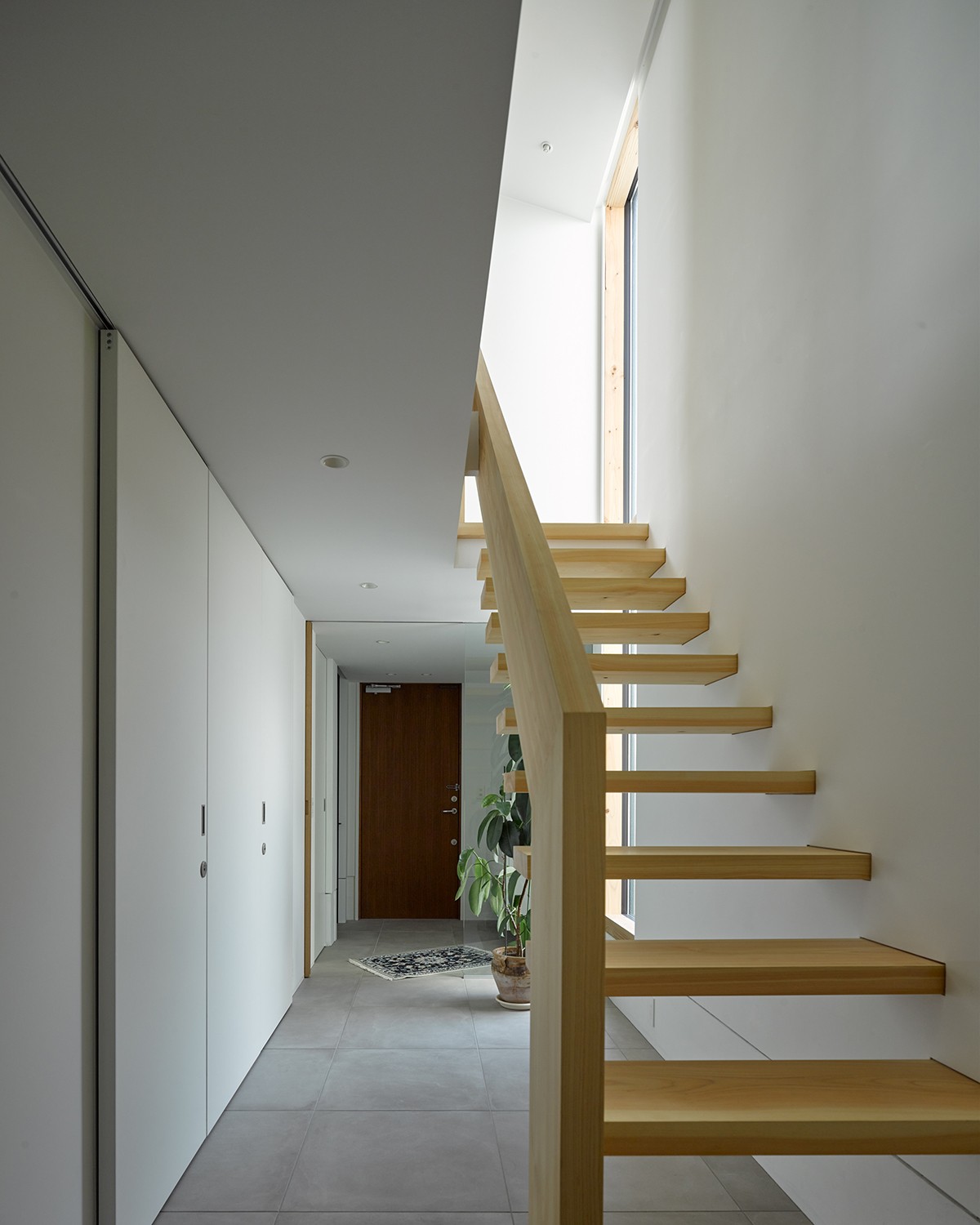 玄関事例：一階廊下．ヒノキ無垢材の階段と土間の連続のようなタイル床の対比（目黒の家〜天空光を取り込む家〜）