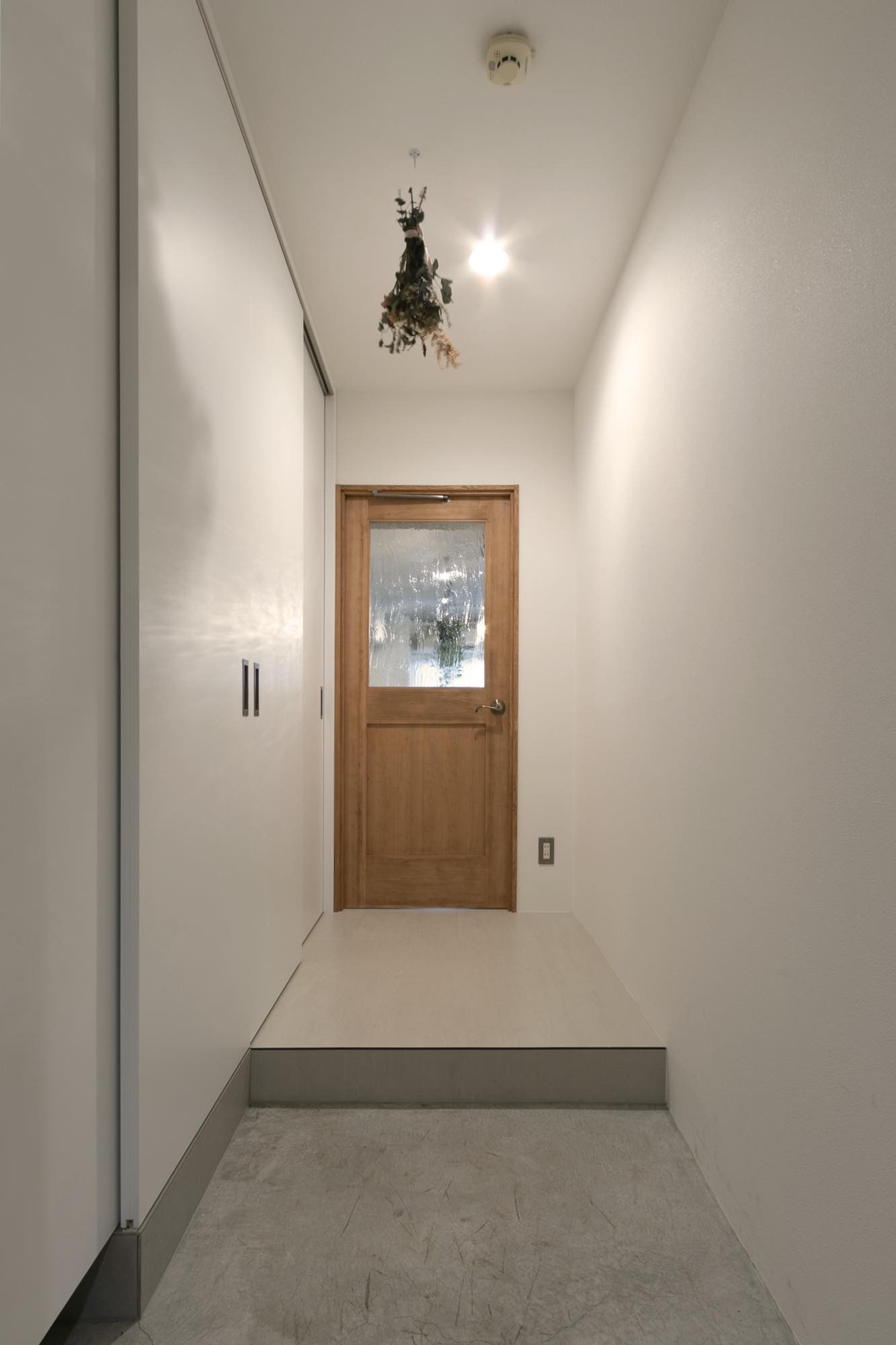 玄関事例：無機質な空間に、木の扉が温かなアクセントをもたらすエントランススペース。（家族の“らしさ”が溶け合う家）